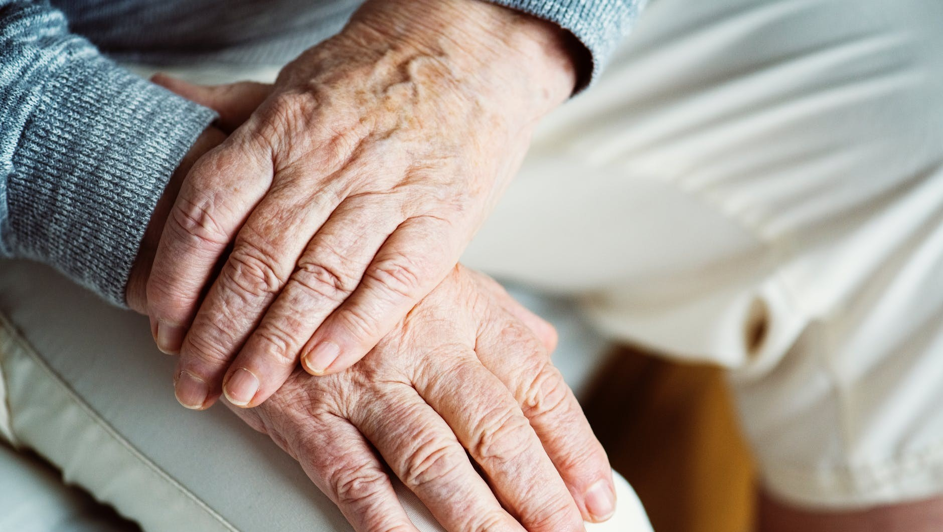 Close-up of an elderly person's hands resting on their lap, symbolizing the importance of long-term care financing. The person is wearing a light gray long-sleeve shirt and light-colored pants.