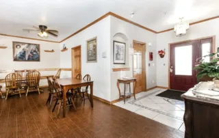 Arvada-gallery-4 A dining area with wooden tables and chairs, wood flooring, wall art, ceiling fan, and a red front door with tiled entryway visible in a bright, well-lit room.