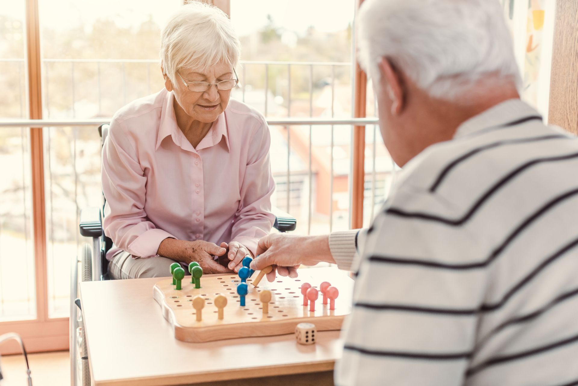 Two elderly people are playing a tabletop board game together in a bright, indoor setting, enjoying their time and fulfilling their senior living needs.