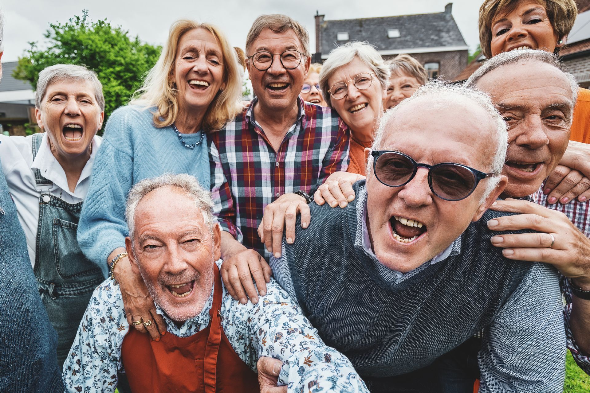 A group of older adults stands closely together outdoors, smiling and laughing at the camera, reflecting the vibrant quality of life often found in assisted living communities.