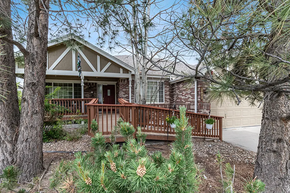 Single-story house with brick and siding exterior, a wooden ramp leading to the front entrance, surrounded by pine trees and landscaped yard.