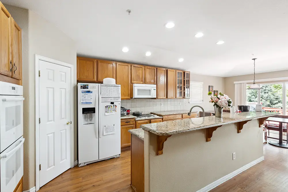 Spacious kitchen with wooden cabinets, granite countertops, white appliances, and a breakfast bar. Sliding glass doors lead to a deck with outdoor seating.