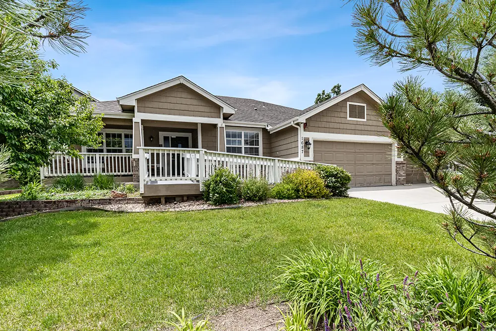 Single-story house with a covered front porch, attached two-car garage, landscaped yard, and green lawn under a blue sky. Single-story house with a covered front porch, attached two-car garage, landscaped yard, and green lawn under a blue sky.