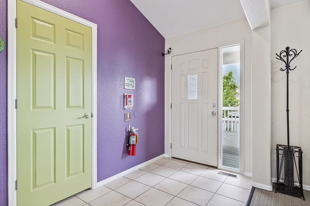 Entryway with a green door, white front door, purple wall, tile floor, fire extinguisher, and a black metal coat rack by a glass panel.