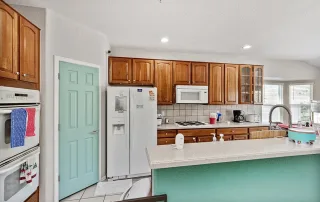 A kitchen in Castle Rock with wooden cabinets, white appliances, a mint green door and island, and various small kitchen items on the counters—ideal for memory care or TBI support environments.