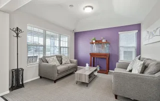 Living room with two gray sofas, a wooden coffee table, and a fish tank on a stand against a purple accent wall—perfect for relaxing or offering TBI Support in Castle Rock, thanks to soothing décor and large windows filled with natural light.