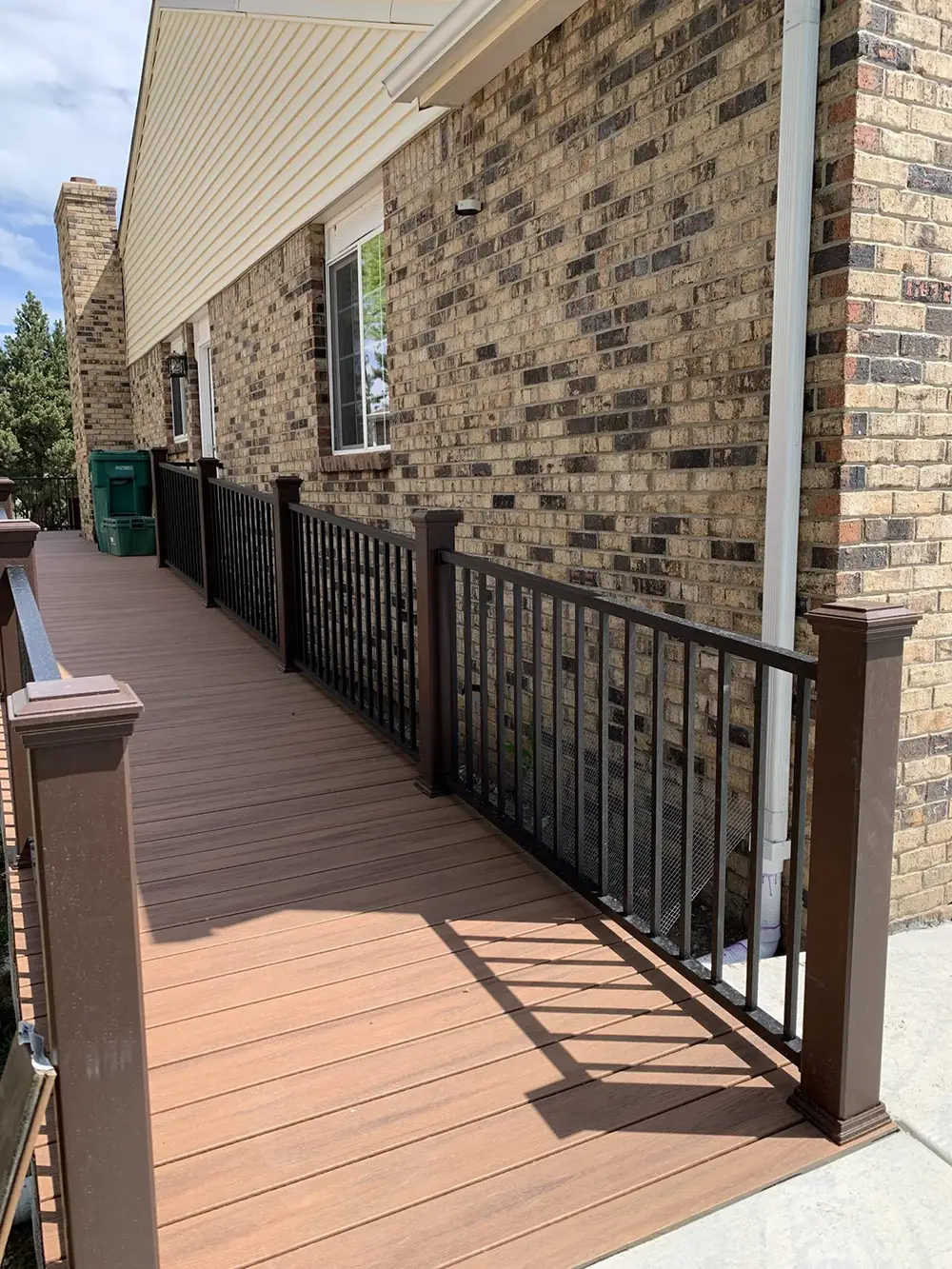 A wooden wheelchair-accessible ramp with dark metal railings is attached to a brick building, leading to a door.