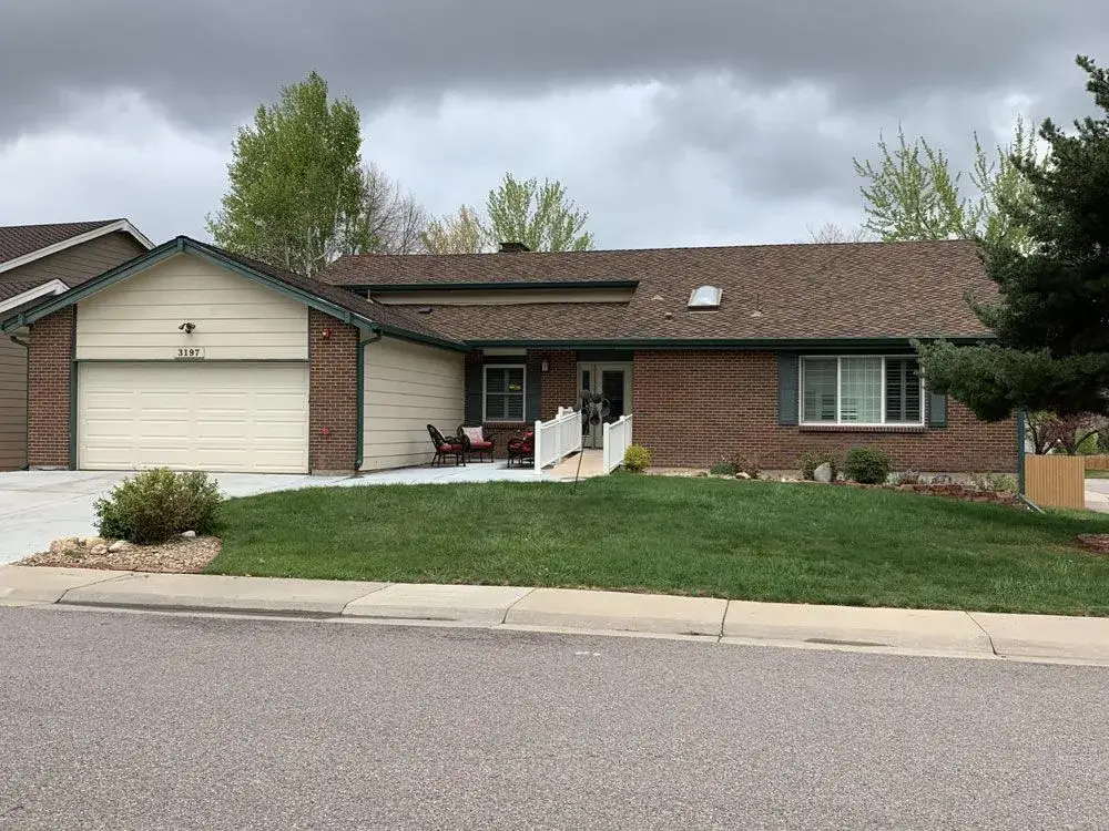 Single-story brick house with a two-car garage, front porch, and well-maintained lawn under a cloudy sky.