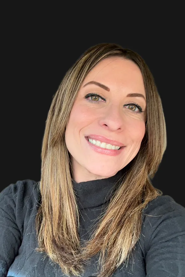 A woman with straight, light brown hair and light eyes, wearing a black turtleneck, smiling in front of a plain black background.