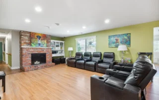 Living room with four black recliners, a brick fireplace, wood flooring, green accent wall, and colorful art above the fireplace and on the wall.