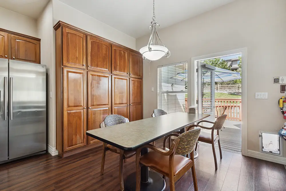 A kitchen with wood cabinets, stainless steel refrigerator, a rectangular dining table with four chairs, and a glass door leading to a deck outside.