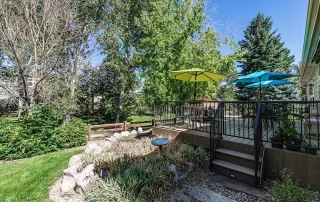 Parker-gallery-1 A backyard patio with tables and colorful umbrellas sits next to a garden with rocks, plants, and trees under a clear blue sky.