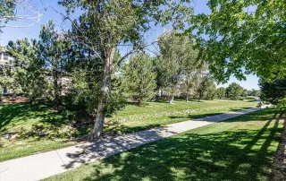 Parker-gallery-2 A paved walking path runs through a grassy area lined with trees on a sunny day.