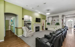 Parker-gallery-3 A living room with black recliner chairs facing a TV above a fireplace, bookshelves, green walls, wood flooring, and an entryway visible in the background.