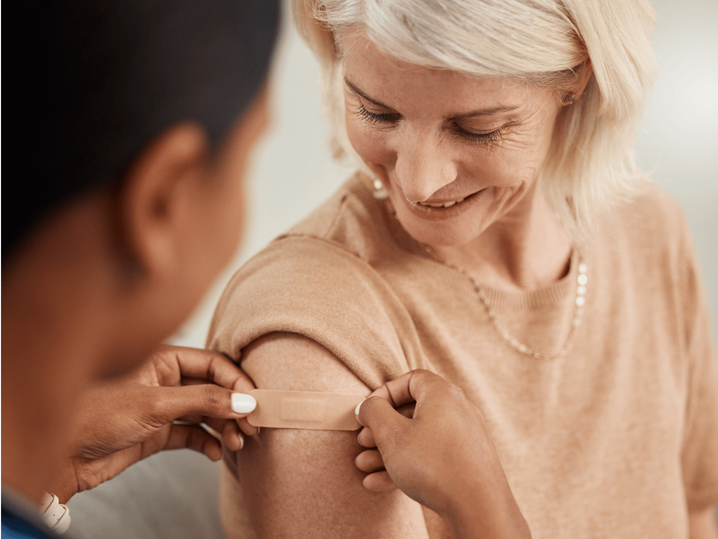 A healthcare worker places a bandage on the upper arm of a smiling woman after receiving her flu vaccination—a vital step for seniors in assisted living.