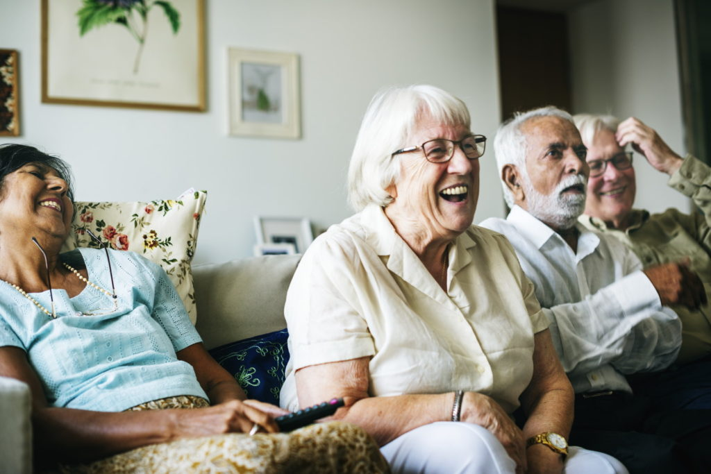 Four older adults sit on a couch indoors in Colorado, smiling and laughing together, with framed artwork hanging on the wall—a warm moment reflecting best quality care.