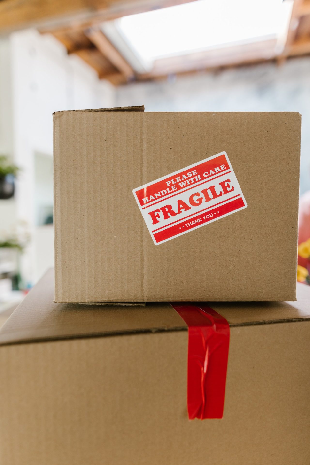 A cardboard box with a red "Fragile: Please Handle With Care" sticker is stacked on another box sealed with red tape—perfect for those seeking assisted living advice or tips for moving with pets safely and securely.