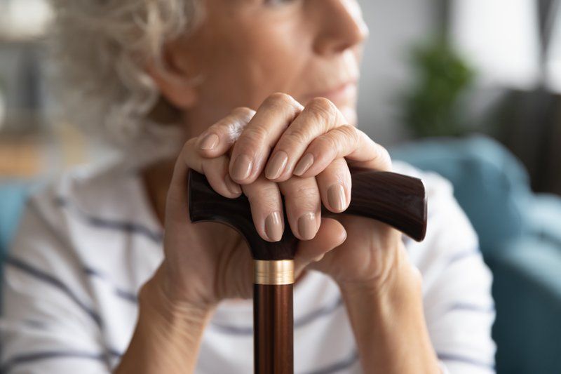Close-up of an older adult resting hands on top of a wooden cane, with the person's face out of focus in the background—a common scene in assisted living communities supporting dementia care.