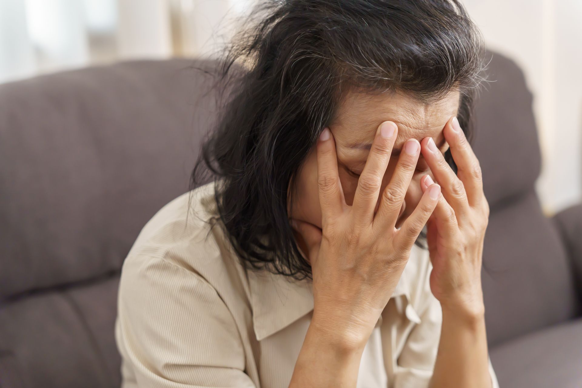 A woman sits on a couch with her head in her hands, appearing stressed or upset—an image that highlights the importance of understanding concussions and their potential long-term effects.