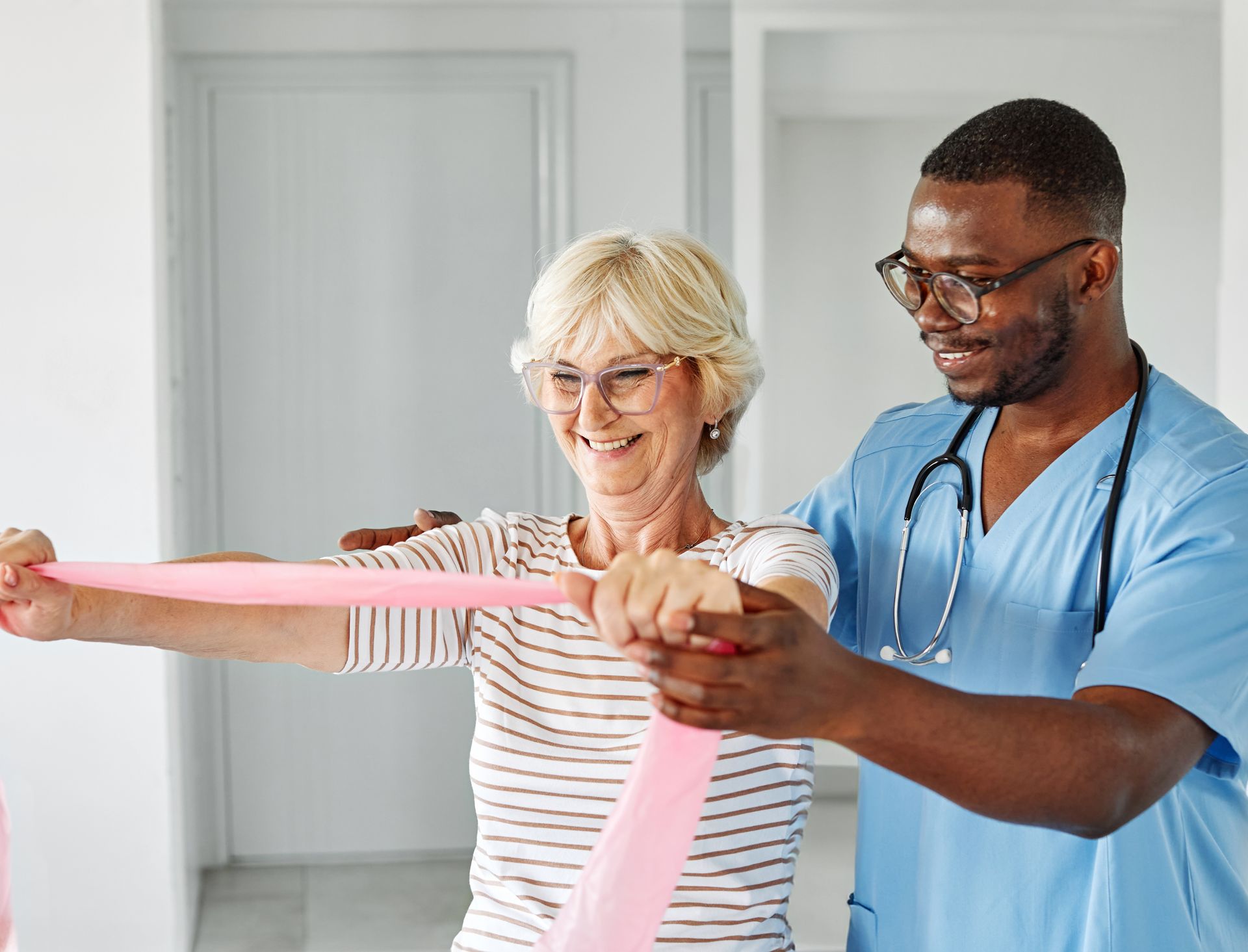 A healthcare professional assists an older woman—one of many brain injury survivors—with resistance band exercises in a bright room, supporting her care plan and recovery.