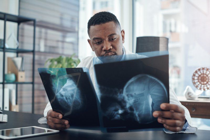 A doctor sits at a desk in a well-lit office, examining two X-ray images to improve understanding of brain injuries and their long-term effects.
