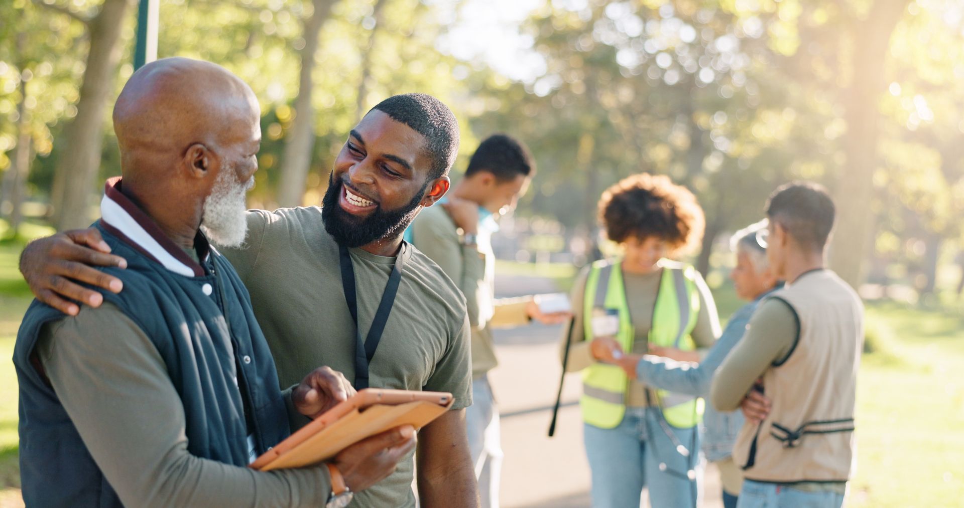 Two seniors talk and smile in a park while holding a clipboard; in the background, others are chatting and sharing decluttering tips and documents.