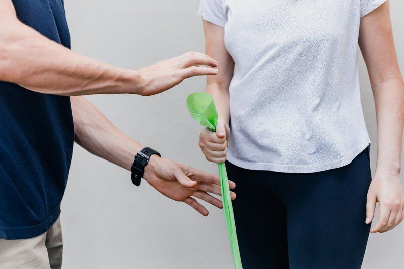Two people stand near each other; one holds a green cane, while the other gestures with their hands as if offering assistance, reflecting support often seen in brain injury rehabilitation.